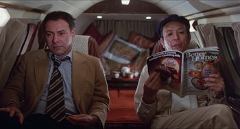 Movie still from “The In-Laws” (1979), directed by Arthur Hiller – Two men sitting on a plane looking at a magazine; Medium shot, Low angle
