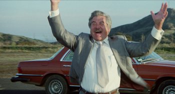 Movie still from “The In-Laws” (1979), directed by Arthur Hiller – An older man in a suit and tie standing in front of a red car; Medium shot, Low angle