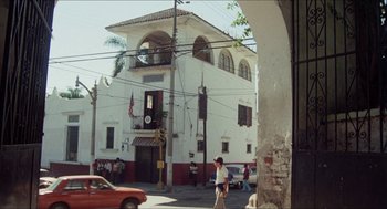 Movie still from “The In-Laws” (1979), directed by Arthur Hiller – A white building with people walking on the sidewalk; Extreme Wide shot, Low angle