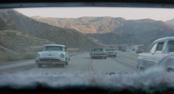 Movie still from “The In-Laws” (1979), directed by Arthur Hiller – A group of cars driving down a road with mountains in the background; Extreme Wide shot, High angle