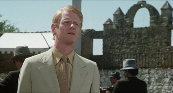 Movie still from “The In-Laws” (1979), directed by Arthur Hiller – A man in a suit and tie standing in front of a stone building; Close Up shot, Low angle