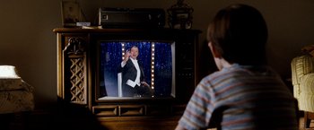 Movie still from “The Incredible Burt Wonderstone” (2013), directed by Don Scardino – A man in a tuxedo is on a television screen; Medium shot, Over the shoulder angle