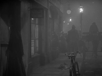 Movie still from “The Informer” (1935), directed by John Ford – A black and white photo of a city street with people walking on the sidewalk; Wide shot, High angle
