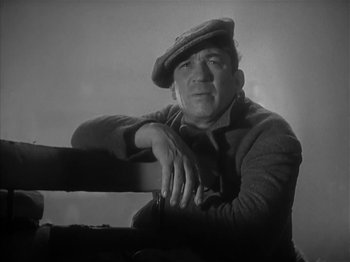 Movie still from “The Informer” (1935), directed by John Ford – An older man wearing a hat leaning on a rail; Medium shot, Low angle