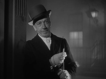 Movie still from “The Informer” (1935), directed by John Ford – A man in a top hat holding a pair of scissors; Close Up shot, Low angle