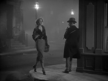 Movie still from “The Informer” (1935), directed by John Ford – A woman walking down a street while talking on the phone; Wide shot, Low angle