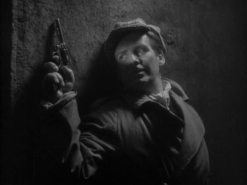 Movie still from “The Informer” (1935), directed by John Ford – A man in a trench coat and hat holding a gun; Close Up shot, Low angle