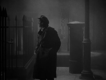 Movie still from “The Informer” (1935), directed by John Ford – A woman in a trench coat standing on a sidewalk; Wide shot, Low angle