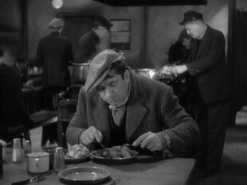 Movie still from “The Informer” (1935), directed by John Ford – A man sitting at a table eating food; Medium shot, High angle