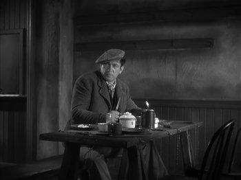 Movie still from “The Informer” (1935), directed by John Ford – A black and white photo of a man sitting at a table; Medium shot, High angle
