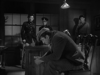 Movie still from “The Informer” (1935), directed by John Ford – A man sitting on top of a wooden bench; Wide shot, High angle
