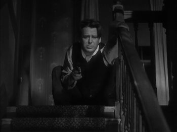 Movie still from “The Informer” (1935), directed by John Ford – A black and white photo of a man sitting on the stairs; Medium shot, Low angle
