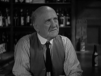 Movie still from “The Informer” (1935), directed by John Ford – An older man sitting at a table in front of bottles; Close Up shot, Over the shoulder angle