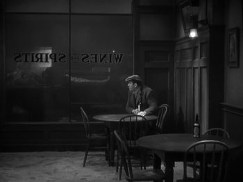 Movie still from “The Informer” (1935), directed by John Ford – A man sitting at a table in front of a window; Wide shot, High angle