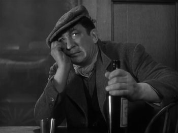 Movie still from “The Informer” (1935), directed by John Ford – An old man sitting at a table with a bottle of beer; Close Up shot, Low angle