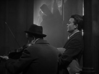 Movie still from “The Informer” (1935), directed by John Ford – Two men are playing musical instruments in front of a window; Medium shot, Low angle