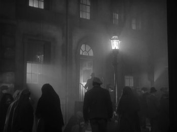 Movie still from “The Informer” (1935), directed by John Ford – A group of people standing in front of a large building; Wide shot, Low angle