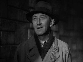 Movie still from “The Informer” (1935), directed by John Ford – A man wearing a hat and a trench coat standing in front of a brick wall; Close Up shot, Low angle