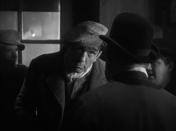 Movie still from “The Informer” (1935), directed by John Ford – A man wearing a hat talking to another man in front of a window; Close Up shot, Over the shoulder angle