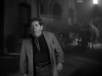 Movie still from “The Informer” (1935), directed by John Ford – A man in a suit and hat standing next to a carriage; Medium shot, Low angle