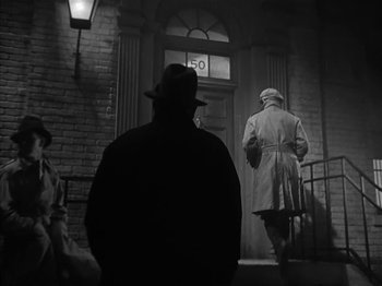 Movie still from “The Informer” (1935), directed by John Ford – A man in a trench coat and hat walking down a street; Wide shot, Low angle
