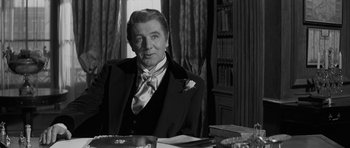 Movie still from “The Innocents” (1961), directed by Jack Clayton – A man in a suit sitting in front of a table; Medium shot, Over the shoulder angle