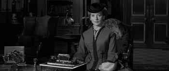Movie still from “The Innocents” (1961), directed by Jack Clayton – A woman sitting in a chair wearing a hat; Medium shot, Low angle