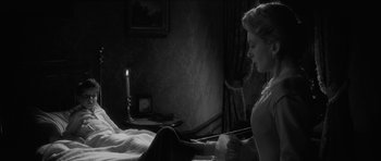 Movie still from “The Innocents” (1961), directed by Jack Clayton – A woman sitting on a bed next to a lit candle; Medium shot, Over the shoulder angle