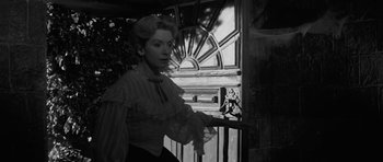 Movie still from “The Innocents” (1961), directed by Jack Clayton – A black and white photo of a woman standing in front of a window; Medium shot, Over the shoulder angle
