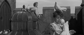 Movie still from “The Innocents” (1961), directed by Jack Clayton – A woman standing on top of a building next to pigeons; Medium shot, Low angle