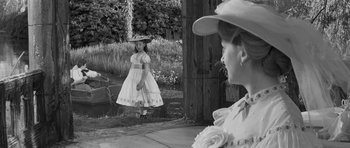 Movie still from “The Innocents” (1961), directed by Jack Clayton – A little girl wearing a dress and a hat standing in front of a woman; Medium shot, Over the shoulder angle