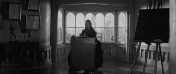 Movie still from “The Innocents” (1961), directed by Jack Clayton – A woman sitting at a desk in front of a large window; Wide shot, Low angle