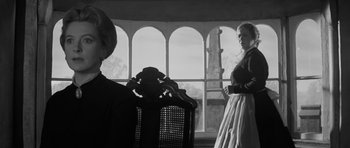 Movie still from “The Innocents” (1961), directed by Jack Clayton – Two women are standing in front of a large window; Medium shot, Over the shoulder angle