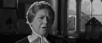 Movie still from “The Innocents” (1961), directed by Jack Clayton – An older woman wearing a head dress and a black jacket; Close Up shot, Over the shoulder angle