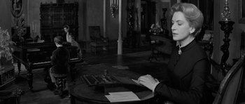 Movie still from “The Innocents” (1961), directed by Jack Clayton – A woman sitting at a table in a living room; Medium shot, High angle