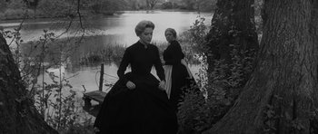 Movie still from “The Innocents” (1961), directed by Jack Clayton – Two women dressed in black standing next to a body of water; Medium shot, High angle