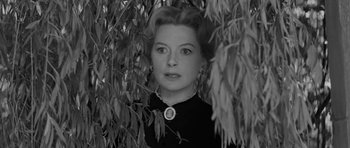 Movie still from “The Innocents” (1961), directed by Jack Clayton – A black - and - white photo of a woman standing in a tree; Close Up shot, Low angle