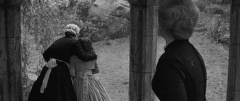 Movie still from “The Innocents” (1961), directed by Jack Clayton – Two women in period dress embracing each other in a wooded area; Medium shot, Over the shoulder angle