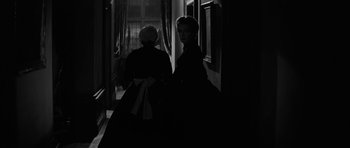 Movie still from “The Innocents” (1961), directed by Jack Clayton – Two women in black dresses are sitting in a dark room; Medium shot, Over the shoulder angle