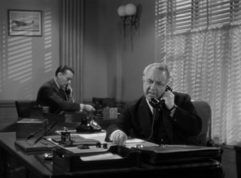 Movie still from “The Invisible Man Returns” (1940), directed by Joe May – Two men sitting at a desk talking on the phone; Medium shot, High angle