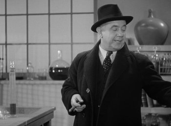 Movie still from “The Invisible Man Returns” (1940), directed by Joe May – A man in a hat and a coat is holding a cigarette; Medium shot, Low angle