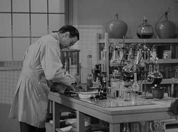 Movie still from “The Invisible Man Returns” (1940), directed by Joe May – A man working in a lab with a lot of glassware on the table; Medium shot, High angle