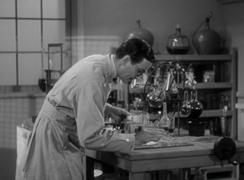 Movie still from “The Invisible Man Returns” (1940), directed by Joe May – A man working in a lab with a microscope; Medium shot, High angle
