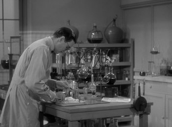 Movie still from “The Invisible Man Returns” (1940), directed by Joe May – A man working in a lab with many glassware on a table; Medium shot, High angle
