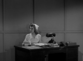 Movie still from “The Invisible Man Returns” (1940), directed by Joe May – A woman sitting at a desk in front of a lamp; Medium shot, Low angle