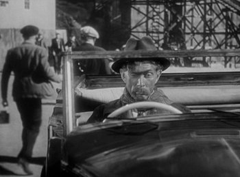 Movie still from “The Invisible Man Returns” (1940), directed by Joe May – A man in a hat driving a car on the street; Medium shot, Over the shoulder angle