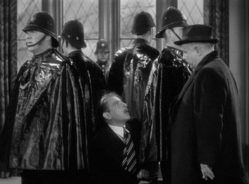 Movie still from “The Invisible Man Returns” (1940), directed by Joe May – A group of men in suits and hats standing next to each other in a room; Medium shot, High angle