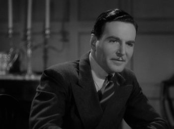 Movie still from “The Invisible Man Returns” (1940), directed by Joe May – A man wearing a suit and tie sitting in front of a table; Close Up shot, Low angle