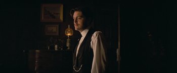 Movie still from “The Invisible Woman” (2013), directed by Ralph Fiennes – A man standing in a dark room wearing a hat; Medium shot, Low angle
