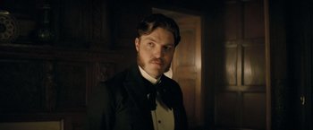 Movie still from “The Invisible Woman” (2013), directed by Ralph Fiennes – A man in a suit and a bow tie in front of a wooden door; Close Up shot, Low angle